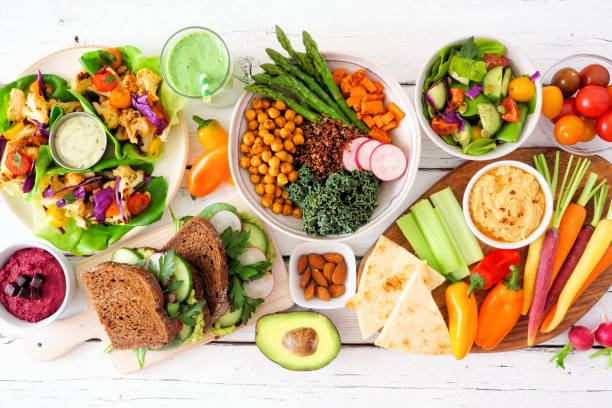 Healthy lunch table scene with nutritious lettuce wraps, Buddha bowl, vegetables, sandwiches, and salad. Overhead view over a white wood background.